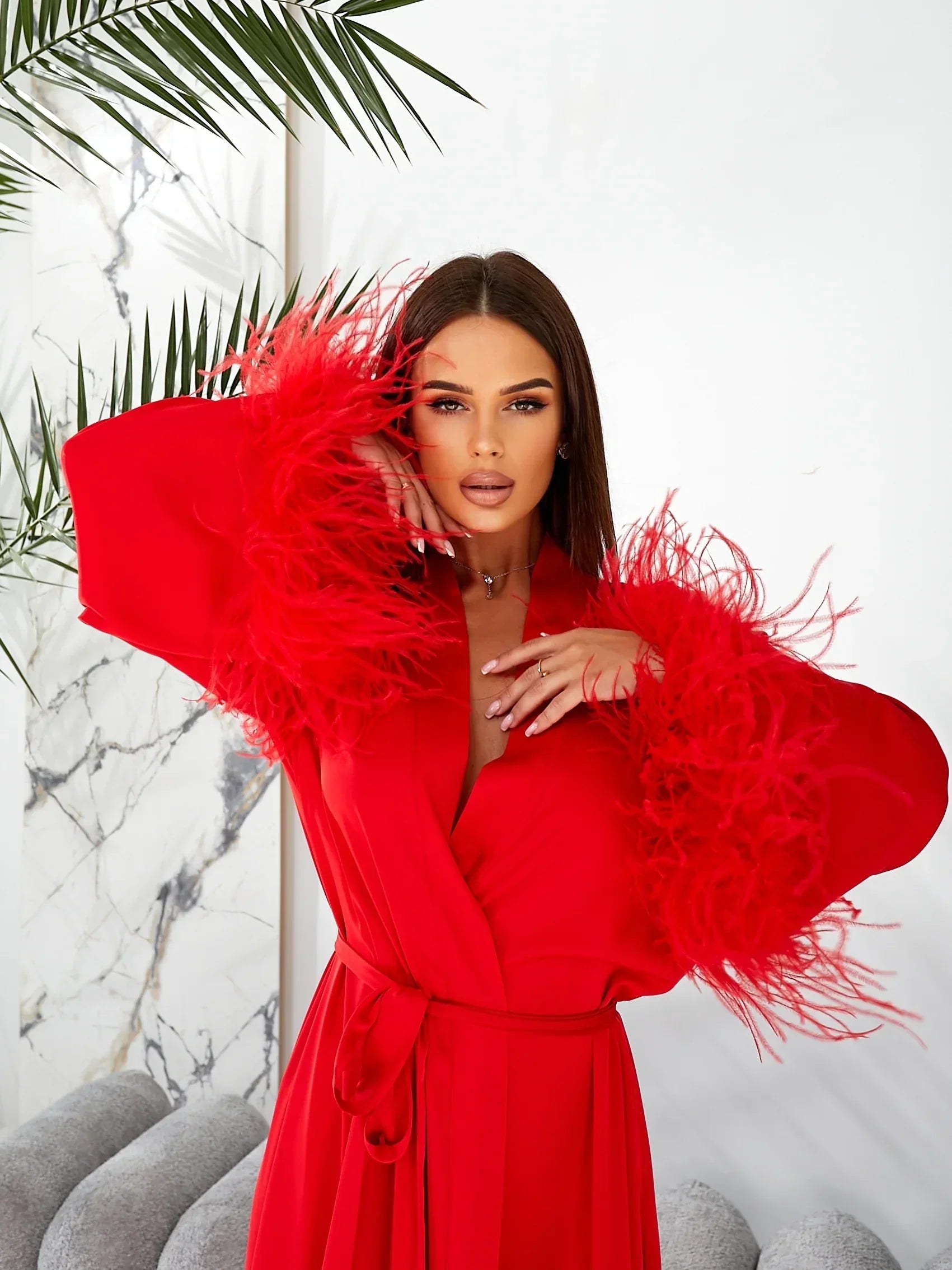 Woman wearing red silk bridal robe with feather-trimmed sleeves, elegant wedding morning style.