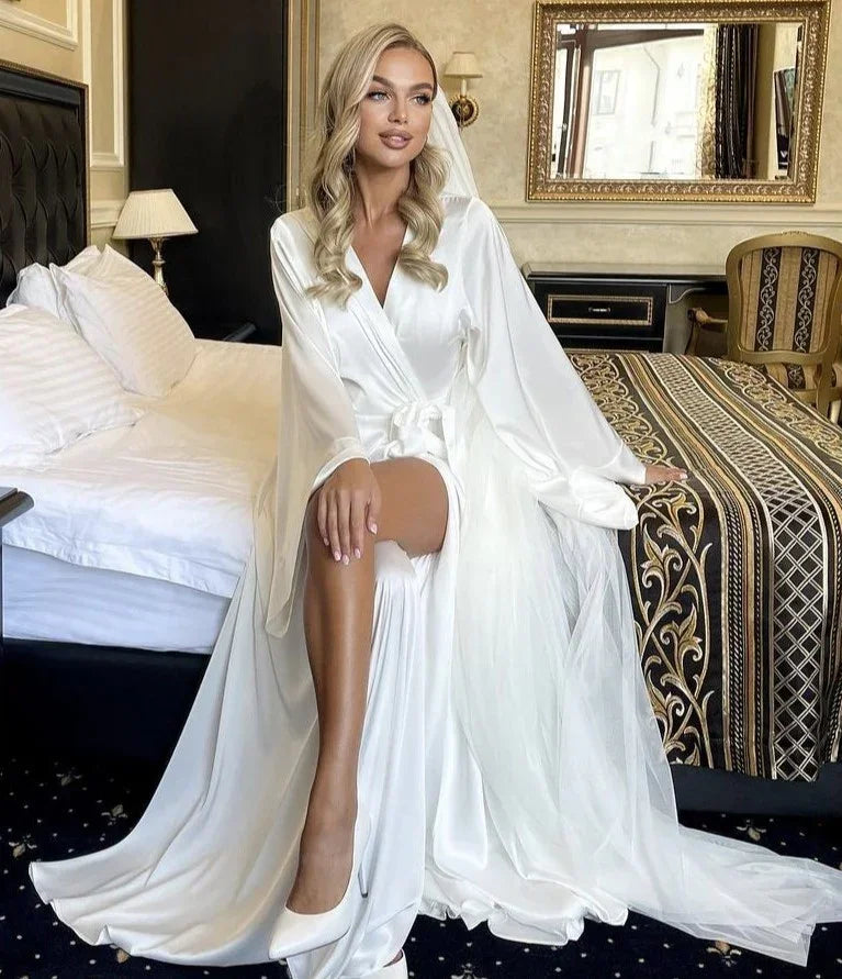 Bride in white silk bridal robe sitting on bed, perfect for wedding morning photos.