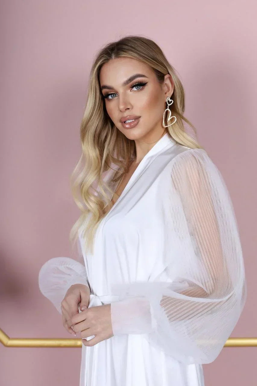 Blonde woman wearing white silk bridal robe with sheer sleeves, perfect for wedding morning.
